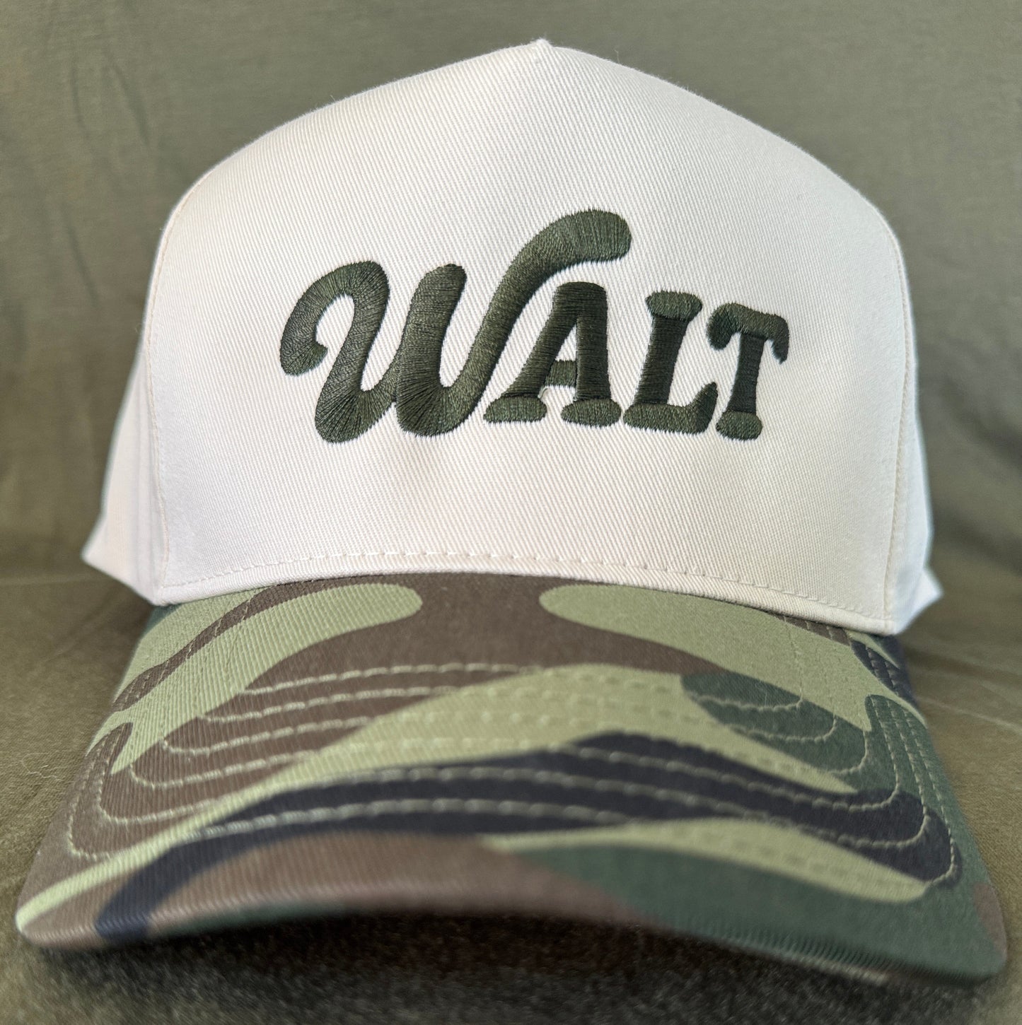 White cap with green embroidered 'WALT' text and camouflage pattern bill