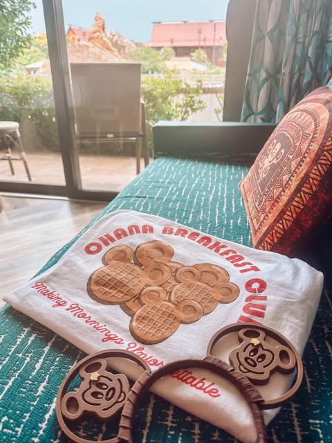 Disney-inspired Ohana Breakfast Club shirt with Mickey waffle design on a bed, resort view outside.