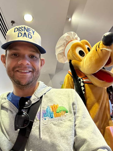 Man in Disney Dad hat and Disney World hoodie posing with Pluto character at theme park