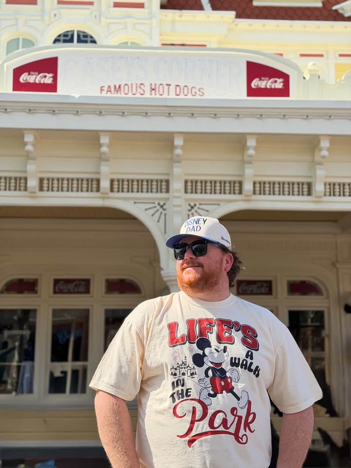 Man wearing Disney Dad hat and Mickey Mouse shirt in front of classic theme park building