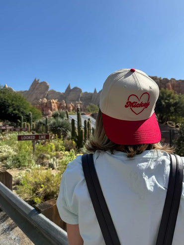 Person wearing Mickey heart baseball cap at theme park with desert landscape and cacti