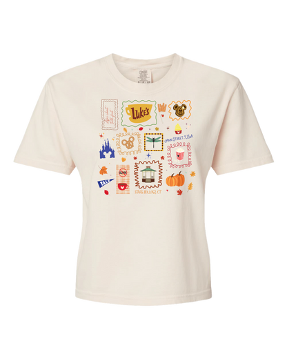 Cream t-shirt with colorful, whimsical icons including Luke's sign, pumpkins, fall leaves, and castle.