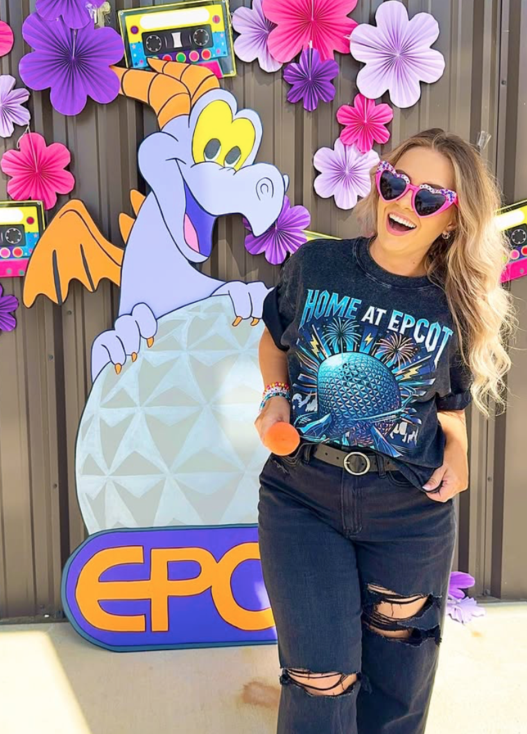 Woman in 'Home at EPCOT' shirt posing by Figment dragon and colorful decorations