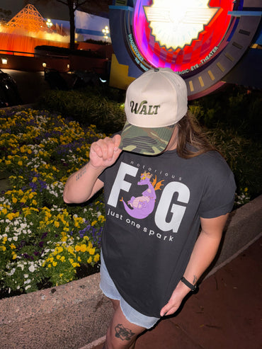 Person in a Walt hat and Figment graphic t-shirt at Epcot, standing near flowers at night.
