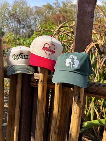 Three Disney-inspired hats on a rustic fence, featuring Walt, Mickey, and Mickey silhouette designs