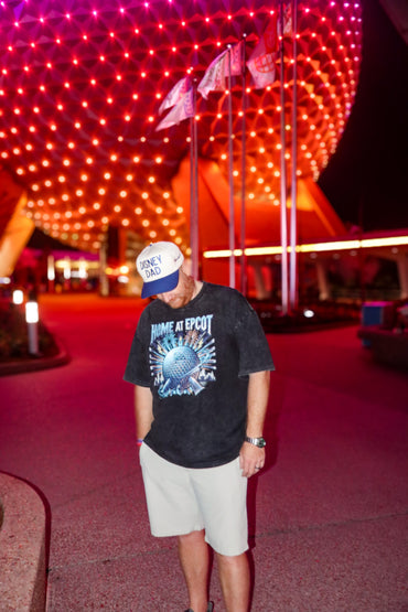 Man wearing 'Home at Epcot' shirt and 'Disney Dad' hat standing at Epcot at night