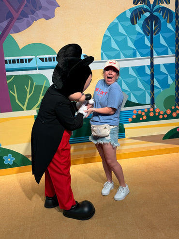 Smiling woman in Disney-inspired outfit meets costumed character at theme park backdrop