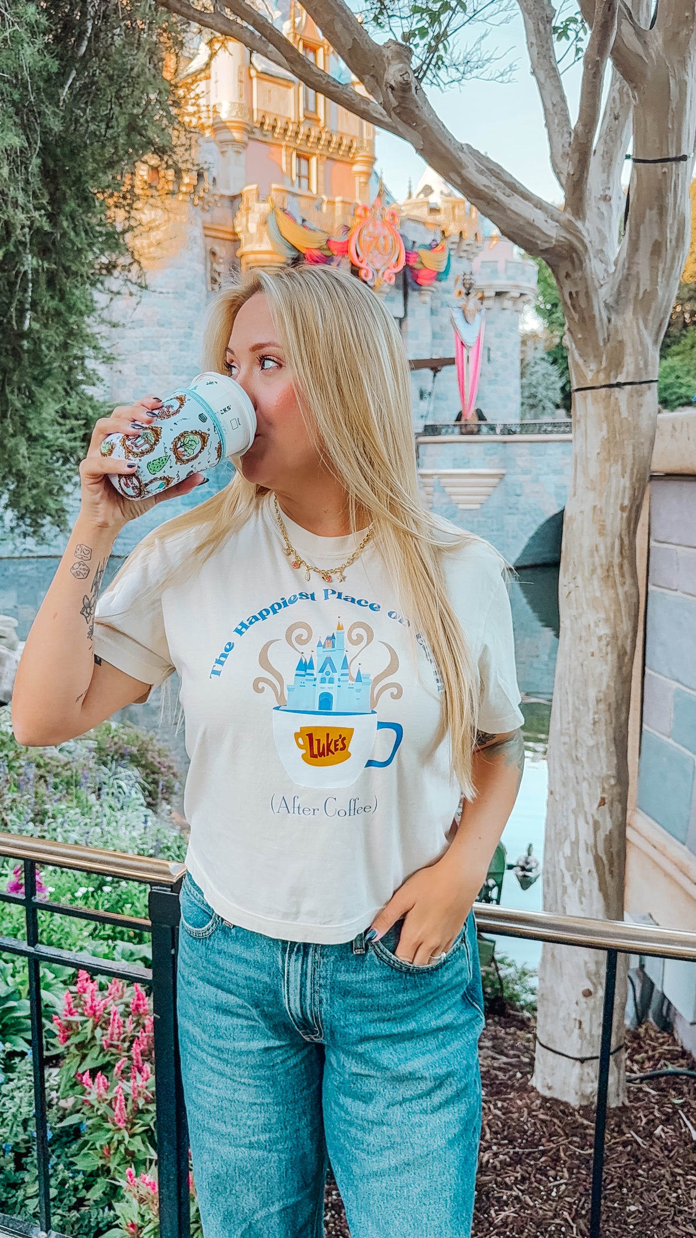 Woman in Disney-inspired graphic tee drinking coffee by castle, casual theme park outfit