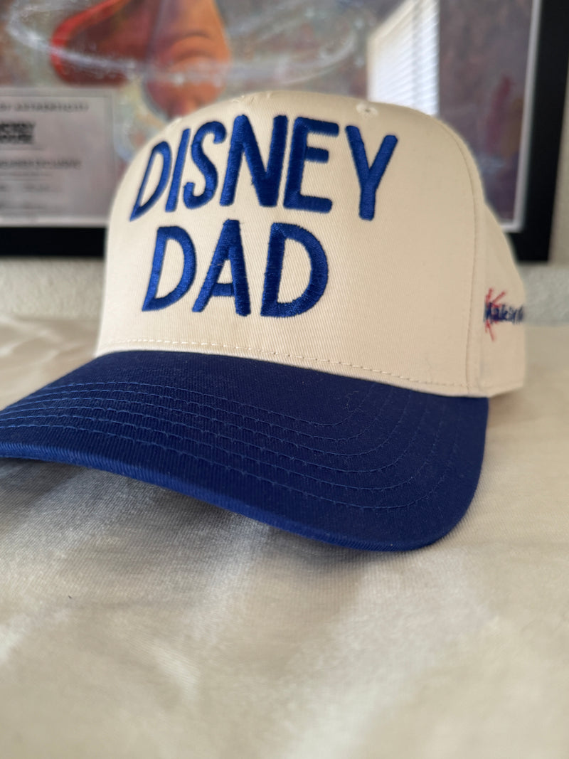 White and blue baseball cap with 'Disney Dad' text embroidered on the front.