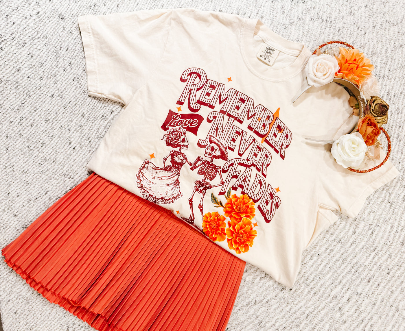 Day of the Dead inspired graphic tee with skeletons, orange pleated skirt, and floral headband