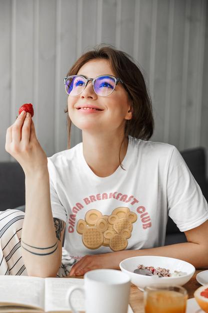 Woman in glasses wearing Ohana Breakfast Club shirt with Mickey-shaped waffle design, eating breakfast