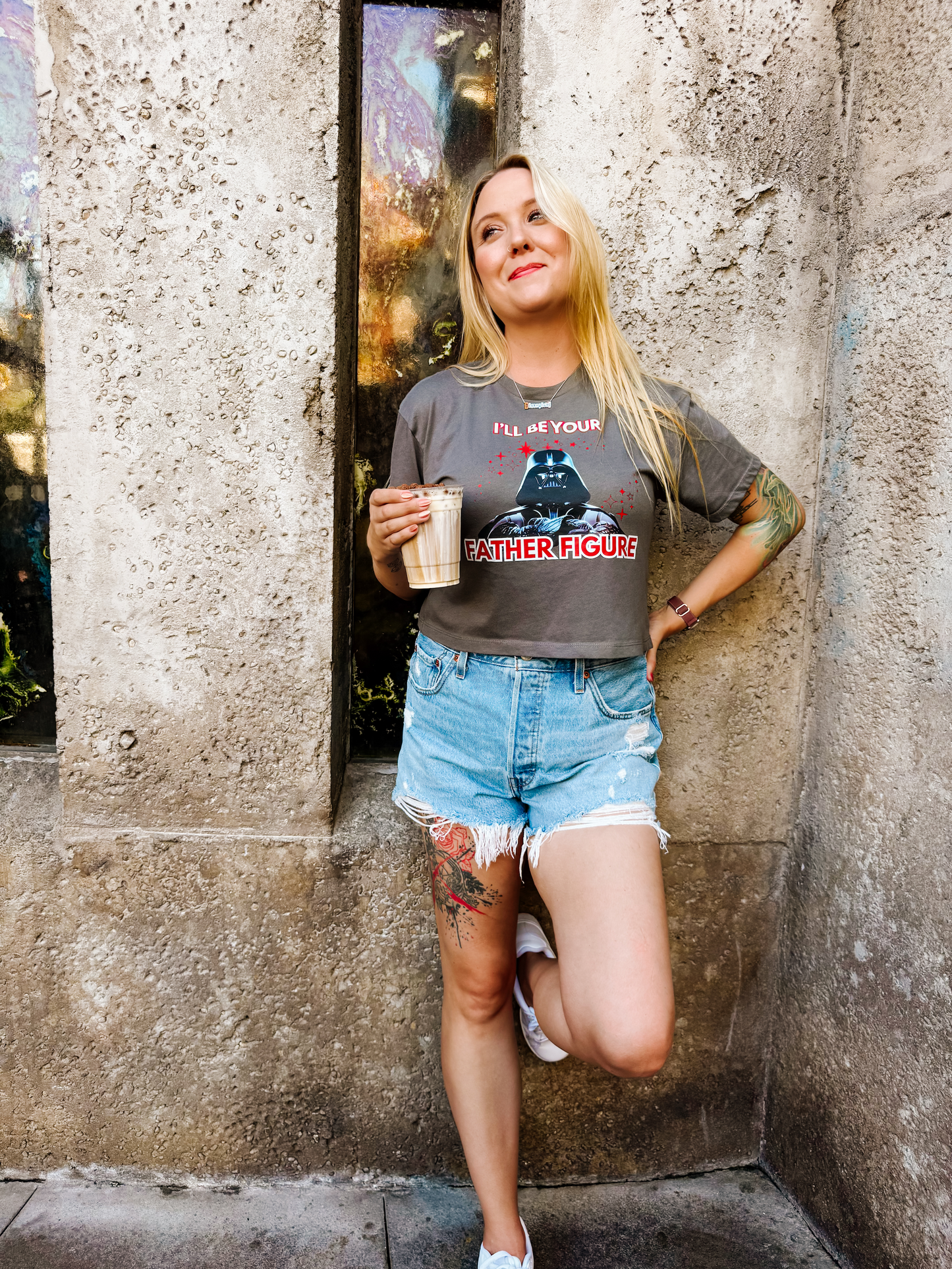 Woman in a Star Wars-inspired 'Father Figure' graphic tee and denim shorts, holding a coffee.