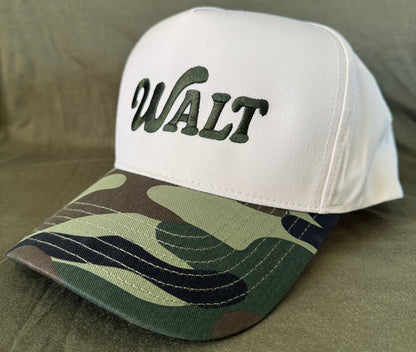 White baseball cap with green 'WALT' embroidery and camouflage bill on fabric background