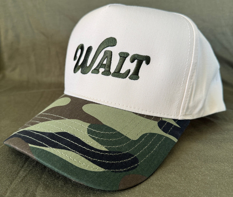 White baseball cap with green 'WALT' embroidery and camouflage bill on fabric background